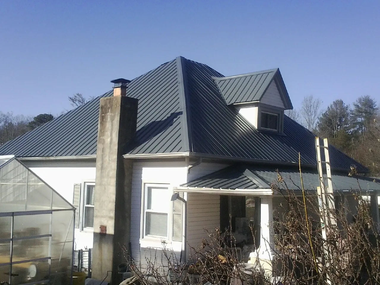 Dark blue standing seam metal roof on a white farmhouse with dormer — Slate & Tile Roof Repair by Roofing Brothers in Estell Manor