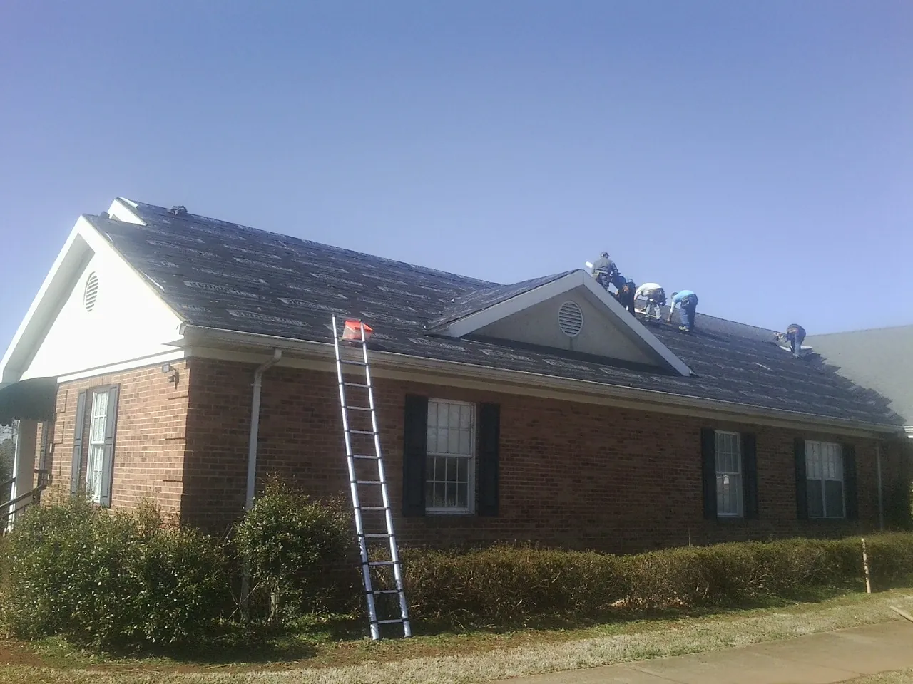 Crew tearing shingles off a brick ranch roof with a ladder set — Metal Roof Repair work by our crew in Estell Manor