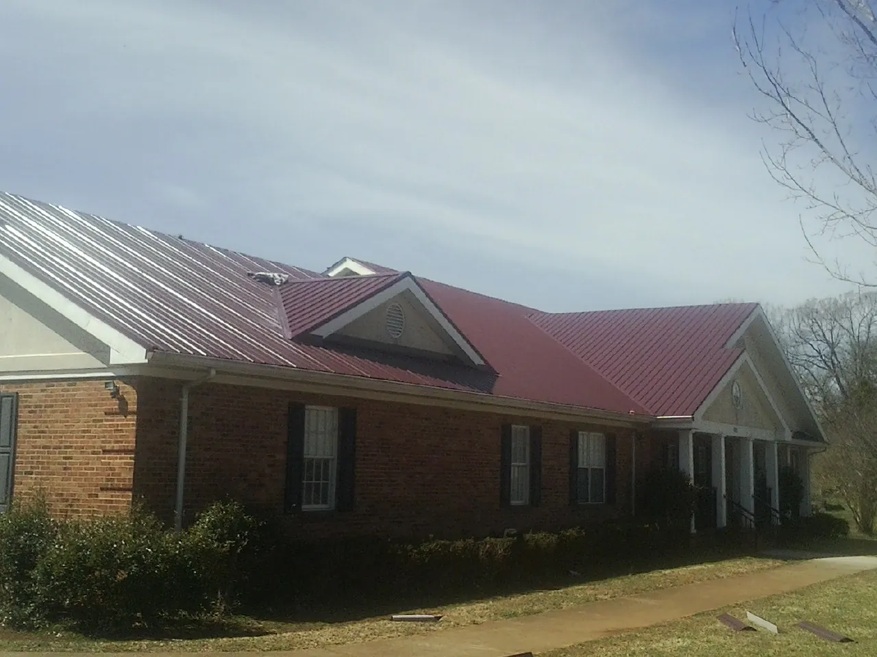 Red metal roof with gabled entries on a long brick building, from a Hail Damage Roof Repair job in Estell Manor