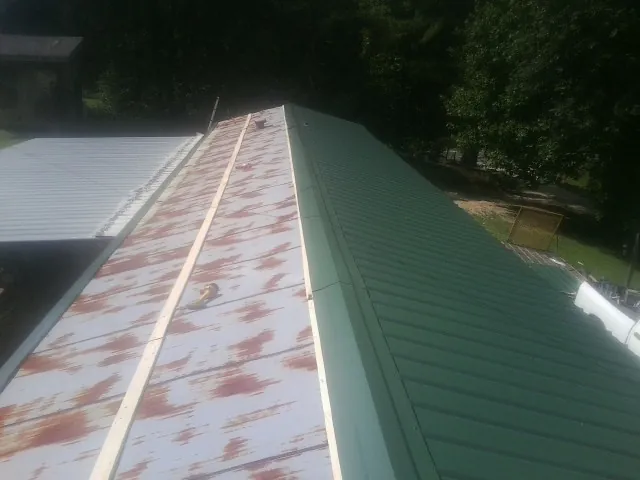 Old rusted panels beside newly installed green metal roofing — Wind Damage Roof Repair by Roofing Brothers in Estell Manor