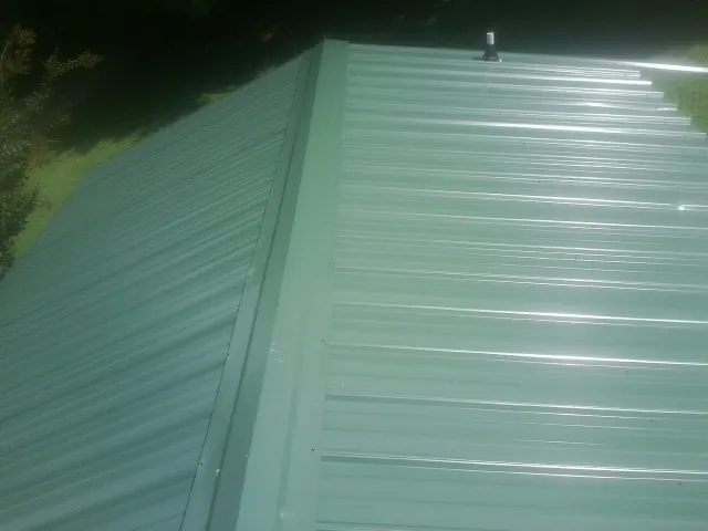 New green metal panels meeting at the ridge of a roof — Flat Roof Repair work by our crew in Estell Manor
