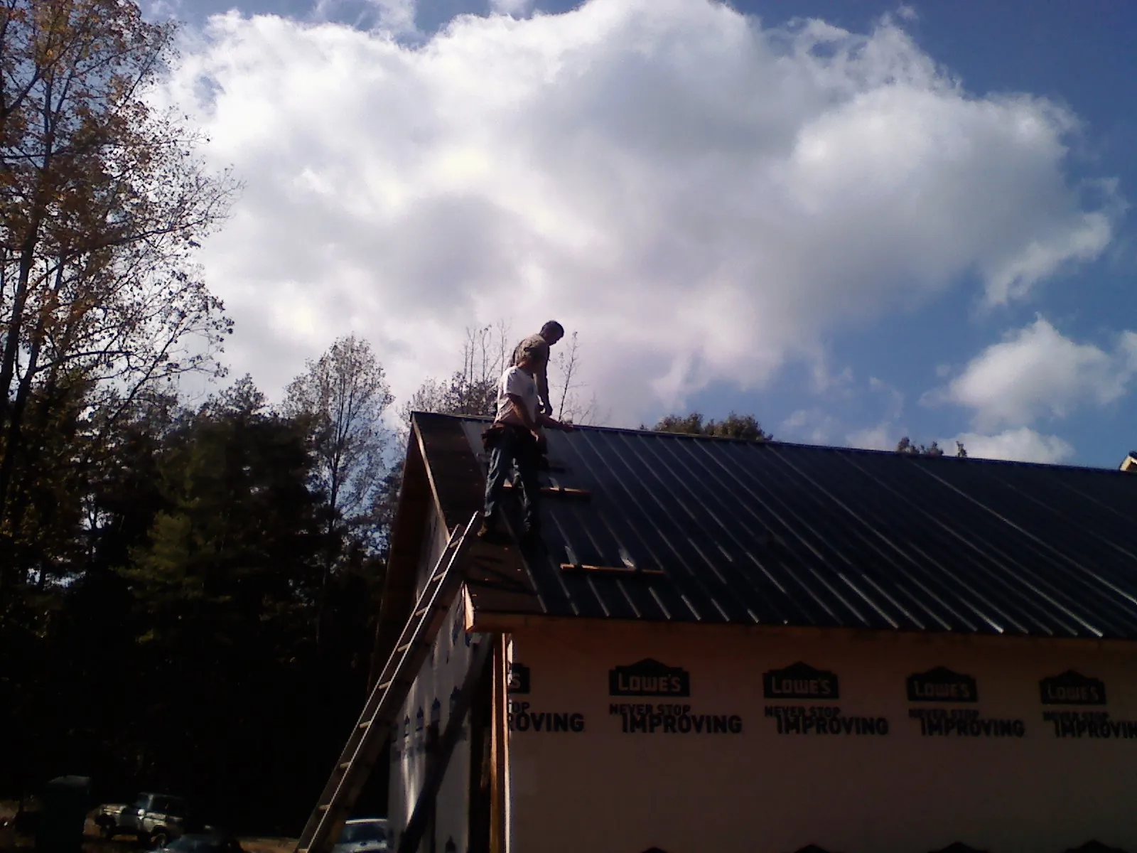 Roofer fastening dark metal panels high against a cloudy sky, from a Roof Inspection job in Estell Manor