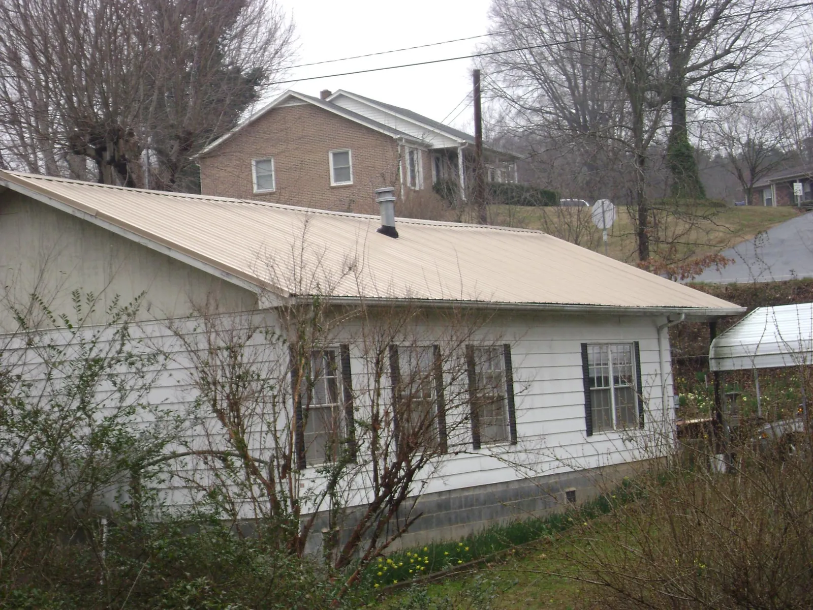 Tan metal roof on a white sided house set into a hillside — Commercial Roofing by Roofing Brothers in Estell Manor