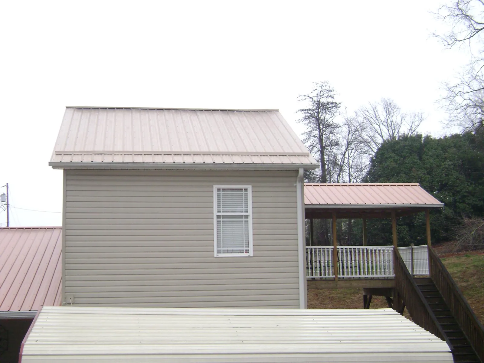 Tan metal roofs on a two story addition and attached porch, from a Roof Replacement job in Estell Manor